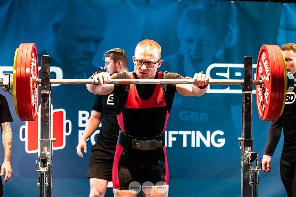 Andrew gripping the bar in the rack, about to take his first squat