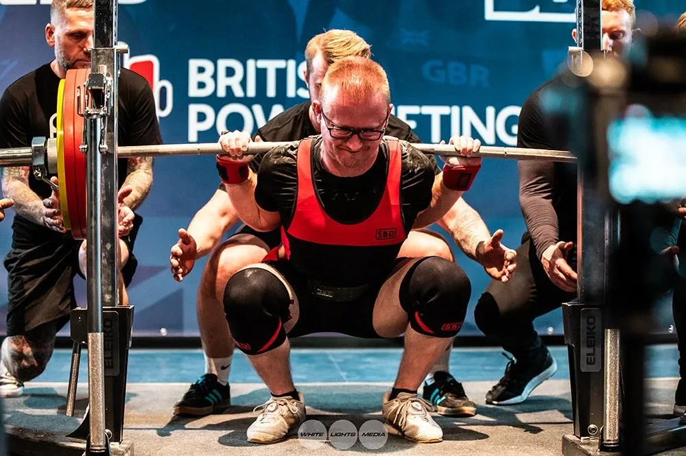 Andrew at the bottom of a squat, with spotters crouched either side