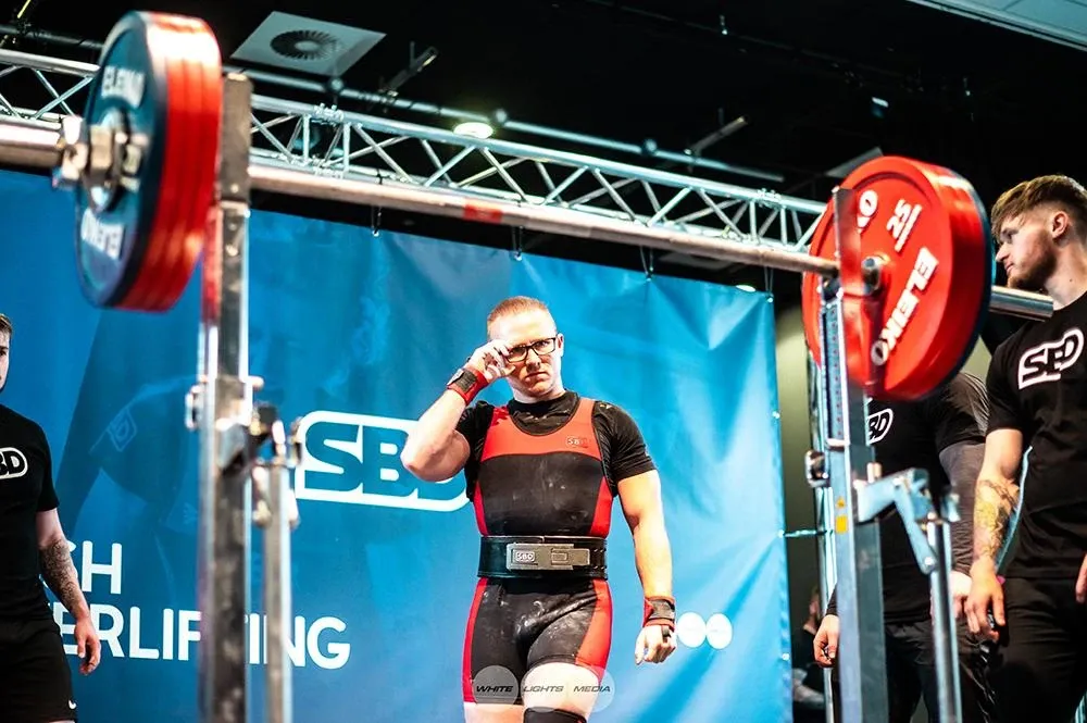 Andrew walking back to the rack for his next squat, adjusting his glasses