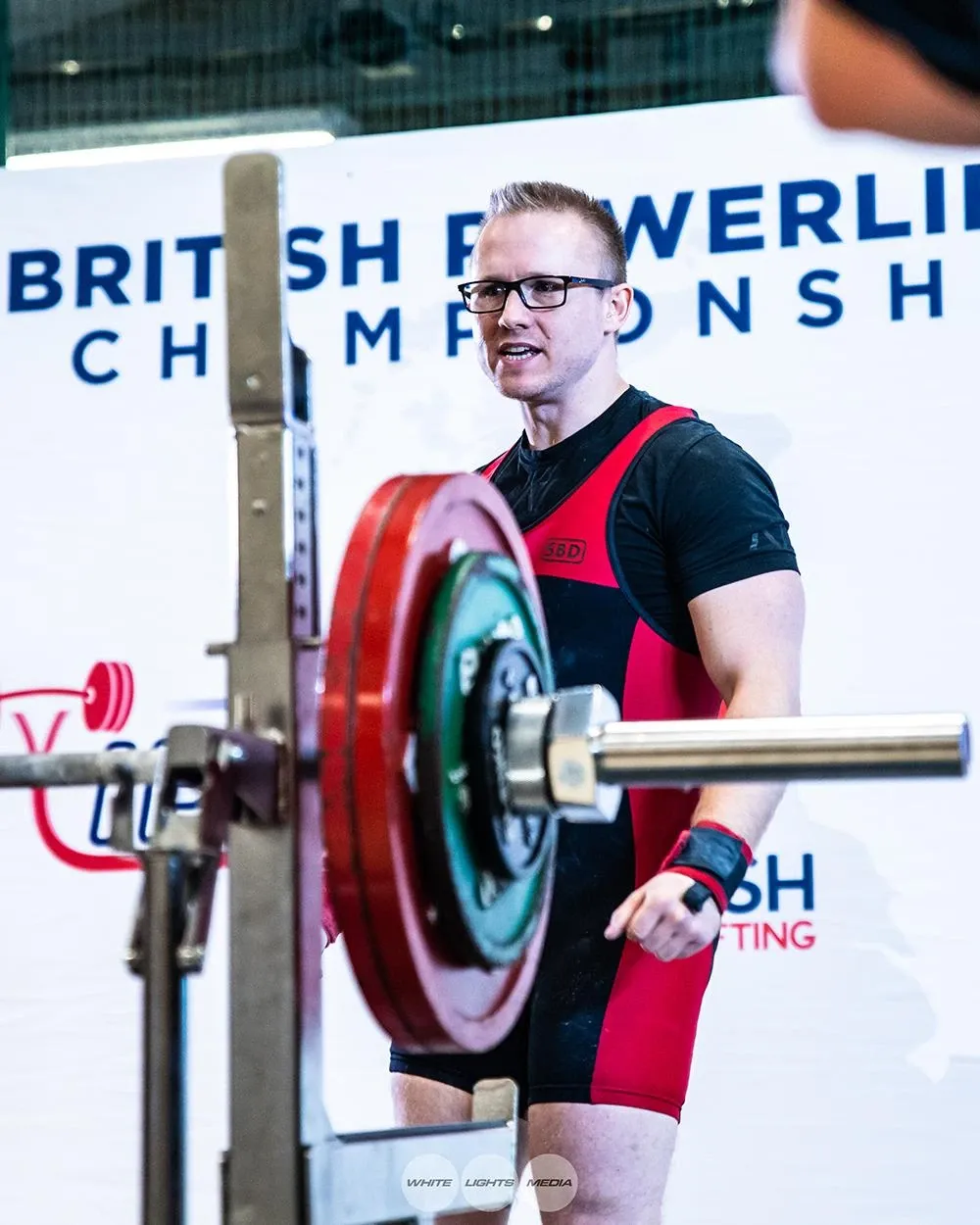 Andrew on the platform in front of the British Powerlifting Championships banner, explaining to the spotters how he wants the centre lift-off