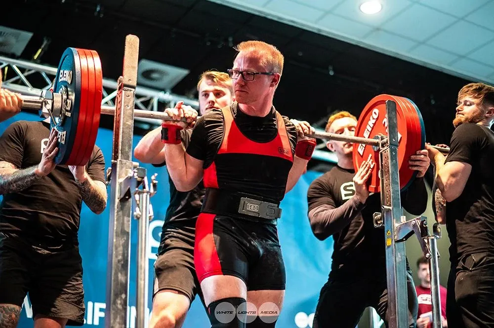 Andrew with the squat bar on his back, stepping out of the rack between spotters