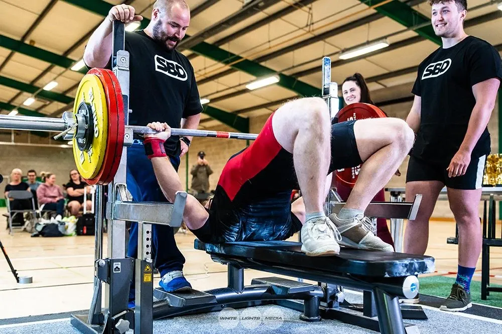 Andrew arching on the bench as he sets up for his 160 kg second attempt, with spotters at each end of the bar