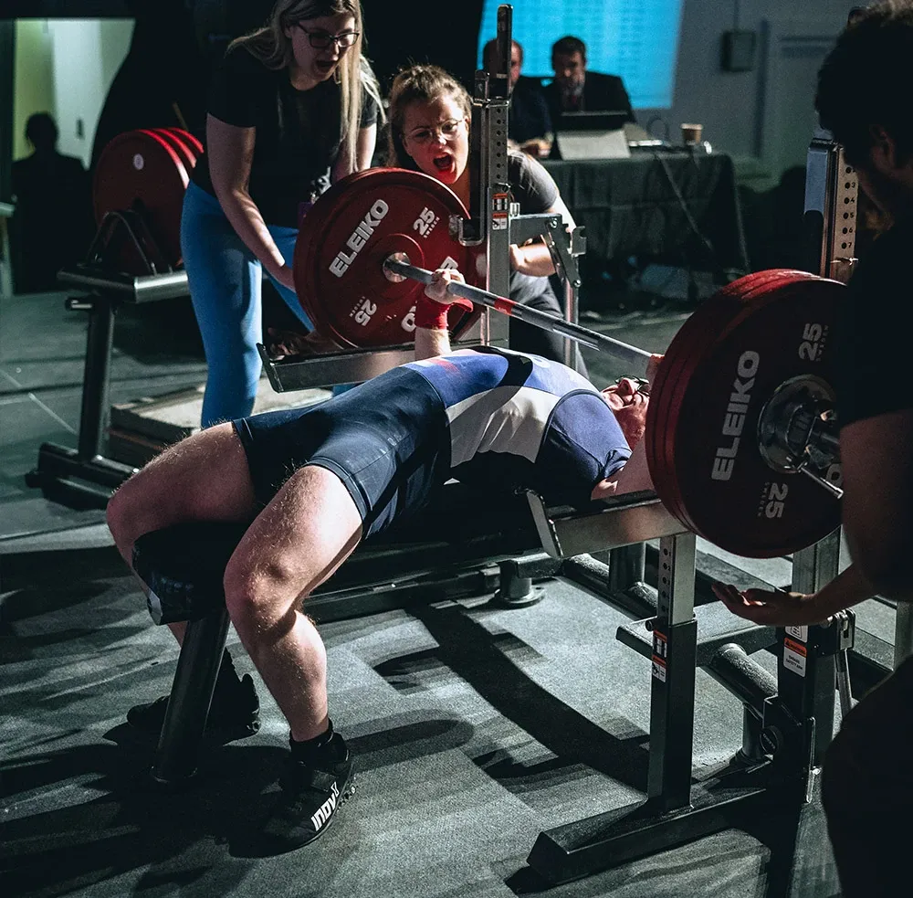 Andrew pressing the bar on his 177.5 kg third attempt while two loaders watch closely