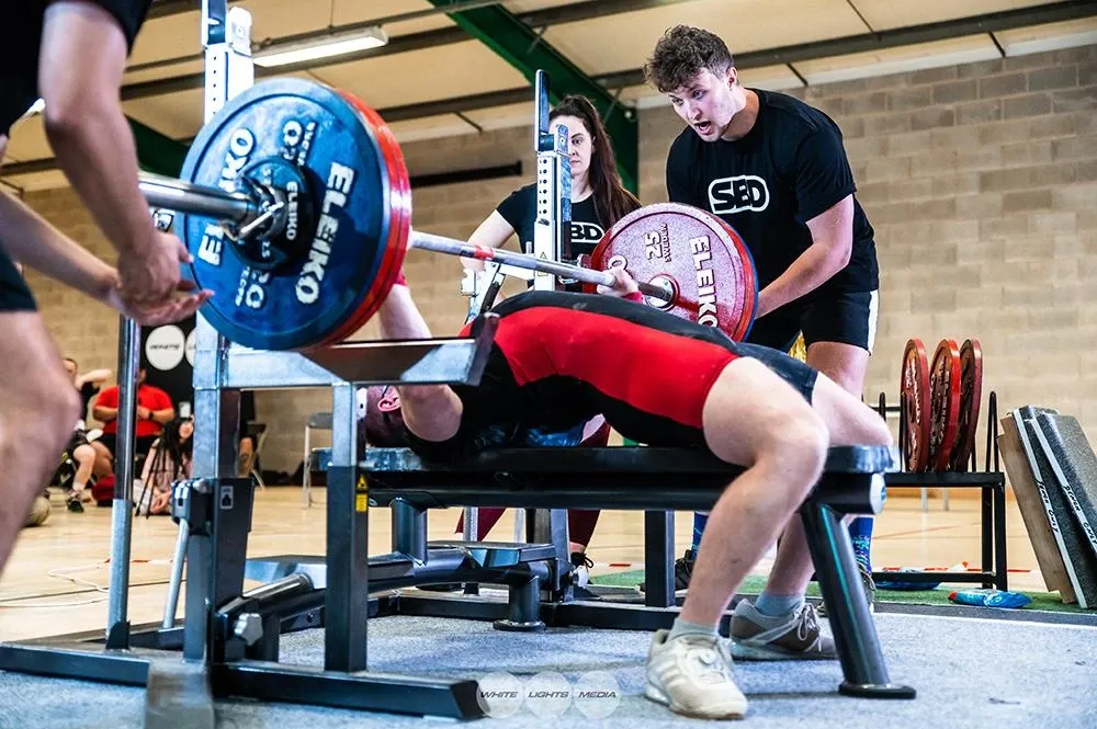 Andrew driving the 170 kg bar up off his chest as the spotters watch