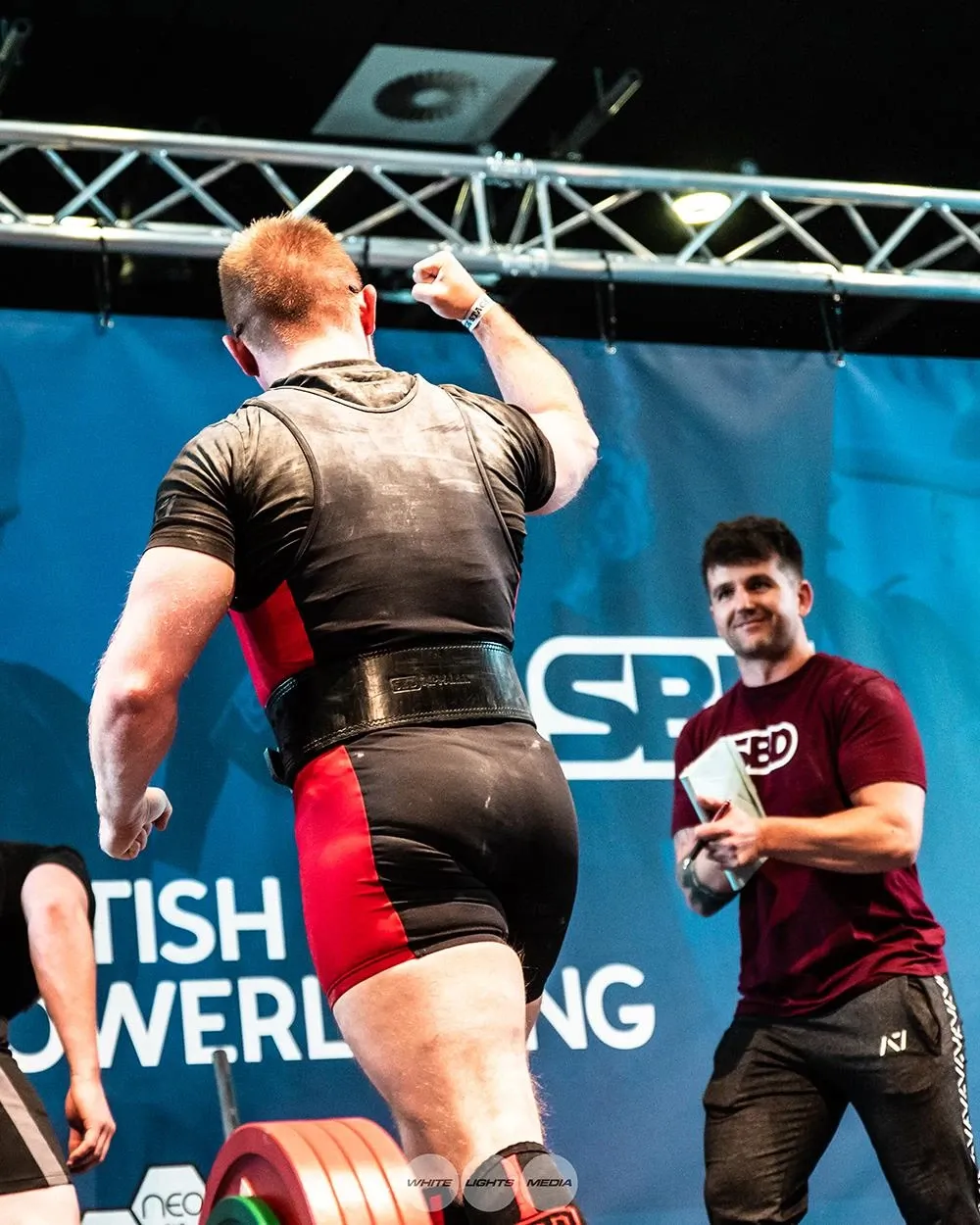 Andrew raising a fist as he walks off the platform, with Luke Rogers smiling beside it, happy with the new total and deadlift
