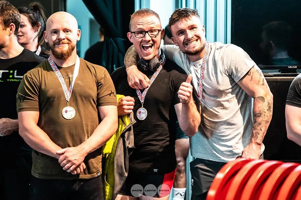 Andrew, Rob and another lifter smiling with medals round their necks at the award ceremony