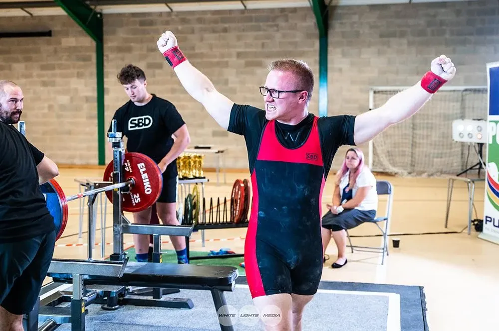 Andrew with both arms raised in celebration after the 170 kg bench press that won the title