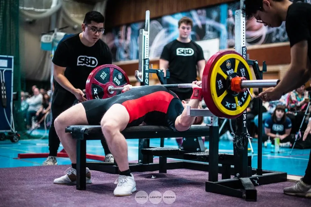 Andrew arched and ready to lift 157.5 kg, with spotters in SBD T-shirts behind him