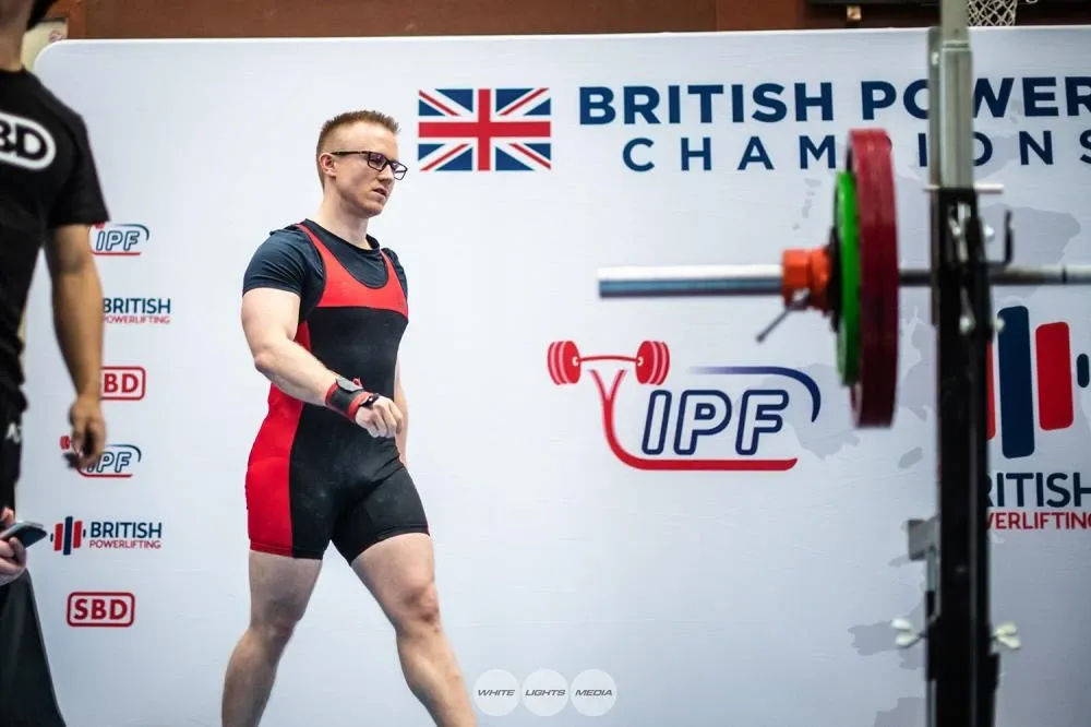 Andrew walking onto the platform in front of the British Powerlifting Championships and IPF banner