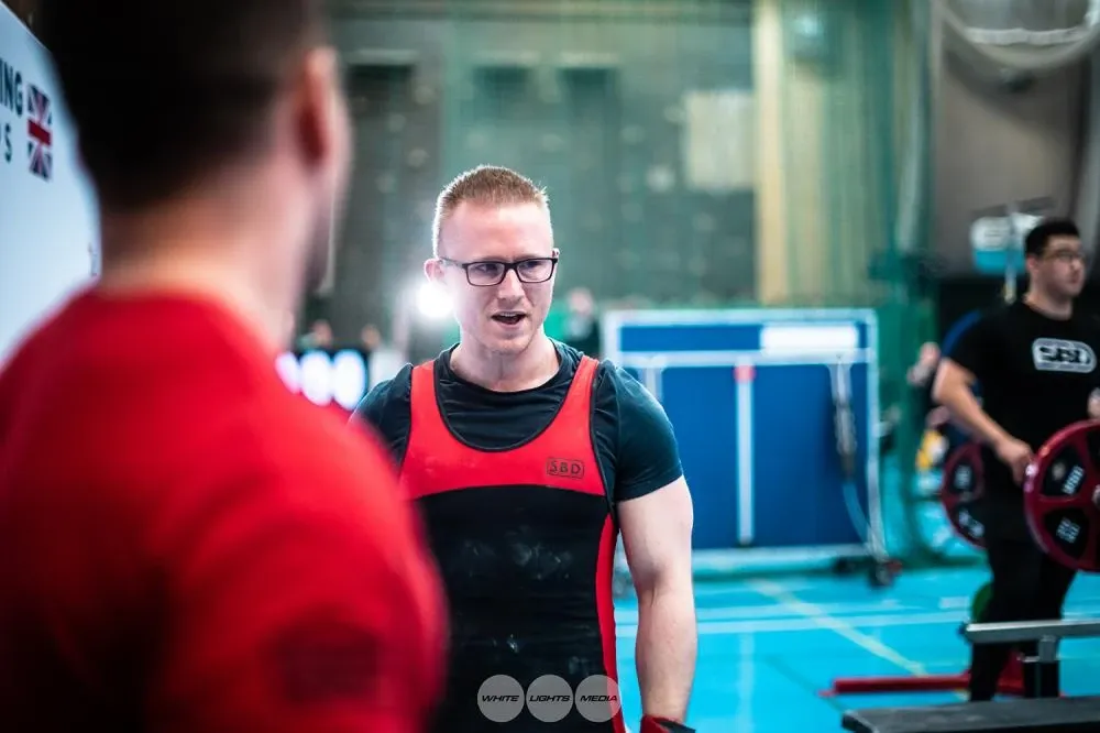 Andrew smiling and talking to his coach, Luke Rogers, beside the platform