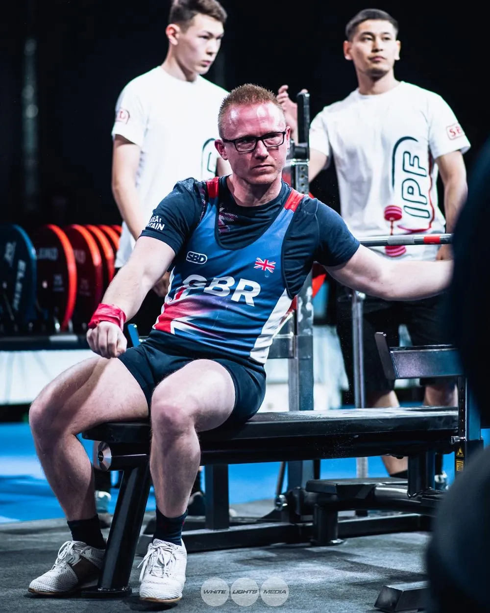 Andrew sitting up on the bench with a loader behind him wearing an IPF T-shirt