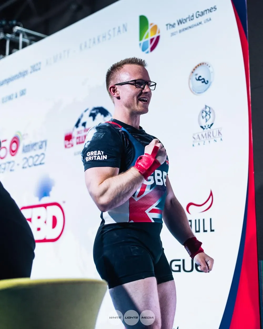 Andrew smiling with his fist to his chest after the 170 kg bench press, in front of the championship backdrop