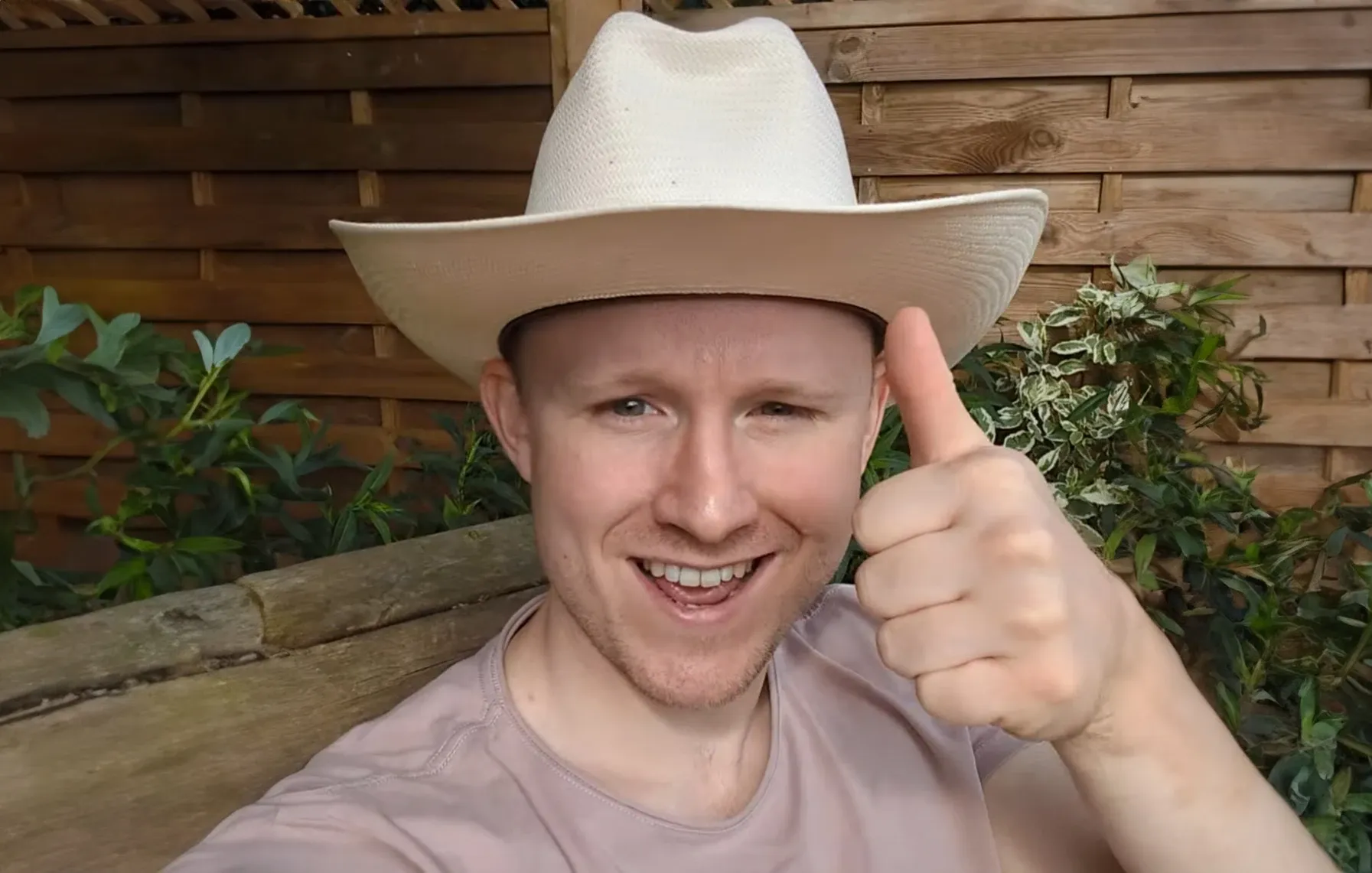 Andrew in a cream cowboy hat, smiling and giving a thumbs up in his garden