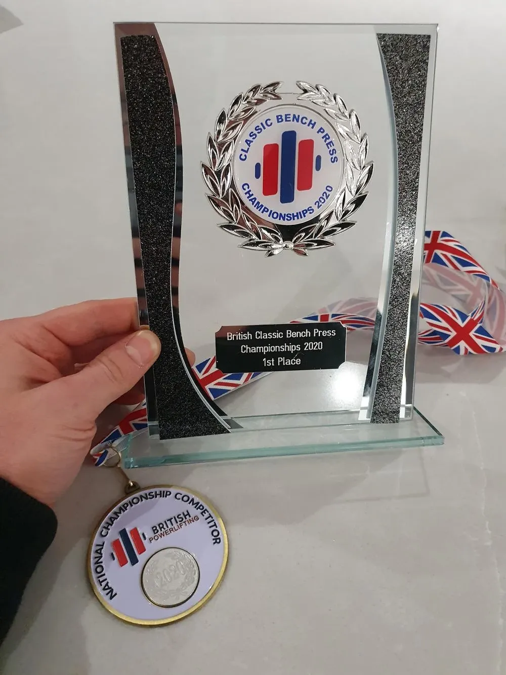 Andrew’s glass first-place trophy from the British Classic Bench Press Championships 2020, with a National Championship Competitor medal