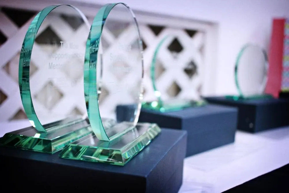 Glass disc trophies on dark presentation boxes, the front two engraved for the Most Supportive Mentor Award