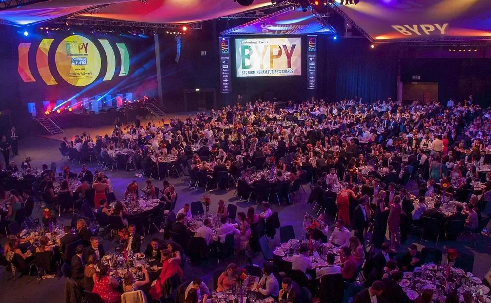 A packed hall of round dinner tables at the BYPY awards, with a big screen reading ‘Celebrating 15 years, BPS Birmingham Future’s Awards’