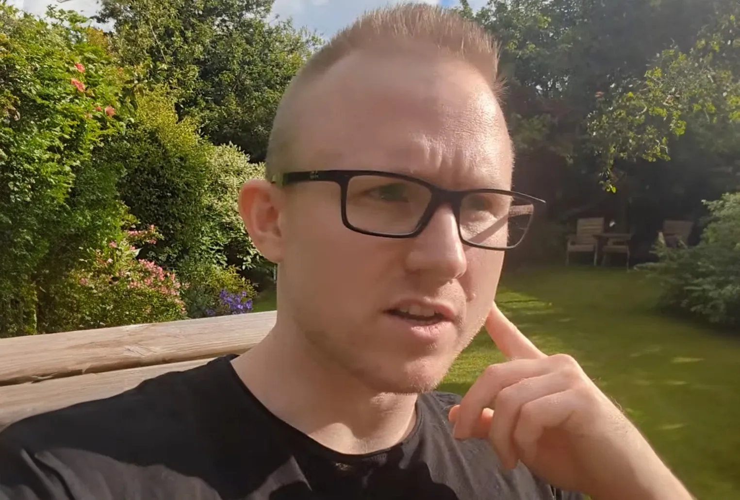 Andrew in his garden, talking to the camera with a finger raised to his temple