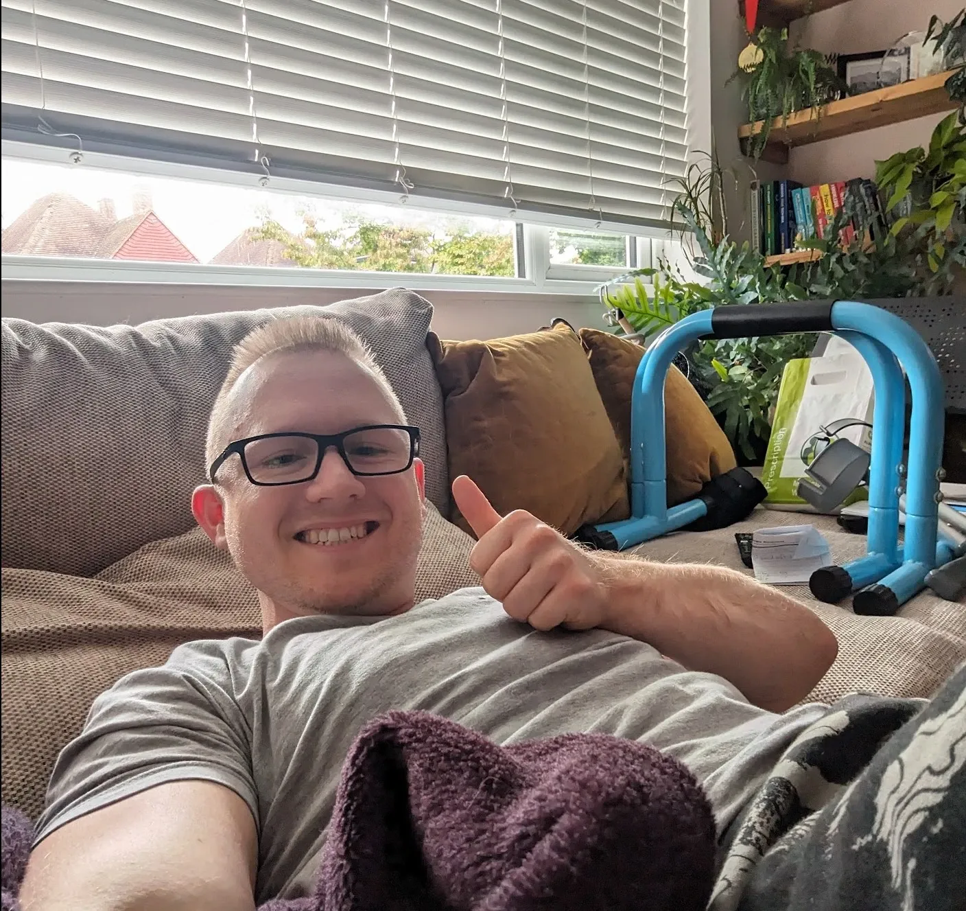 Andrew lying on his sofa at home, smiling and giving a thumbs up