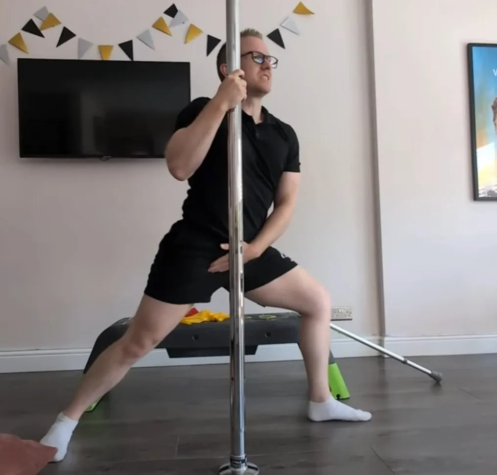 Andrew in a wide side lunge holding a pole, with one hand on his inner thigh to show where the groin pain is