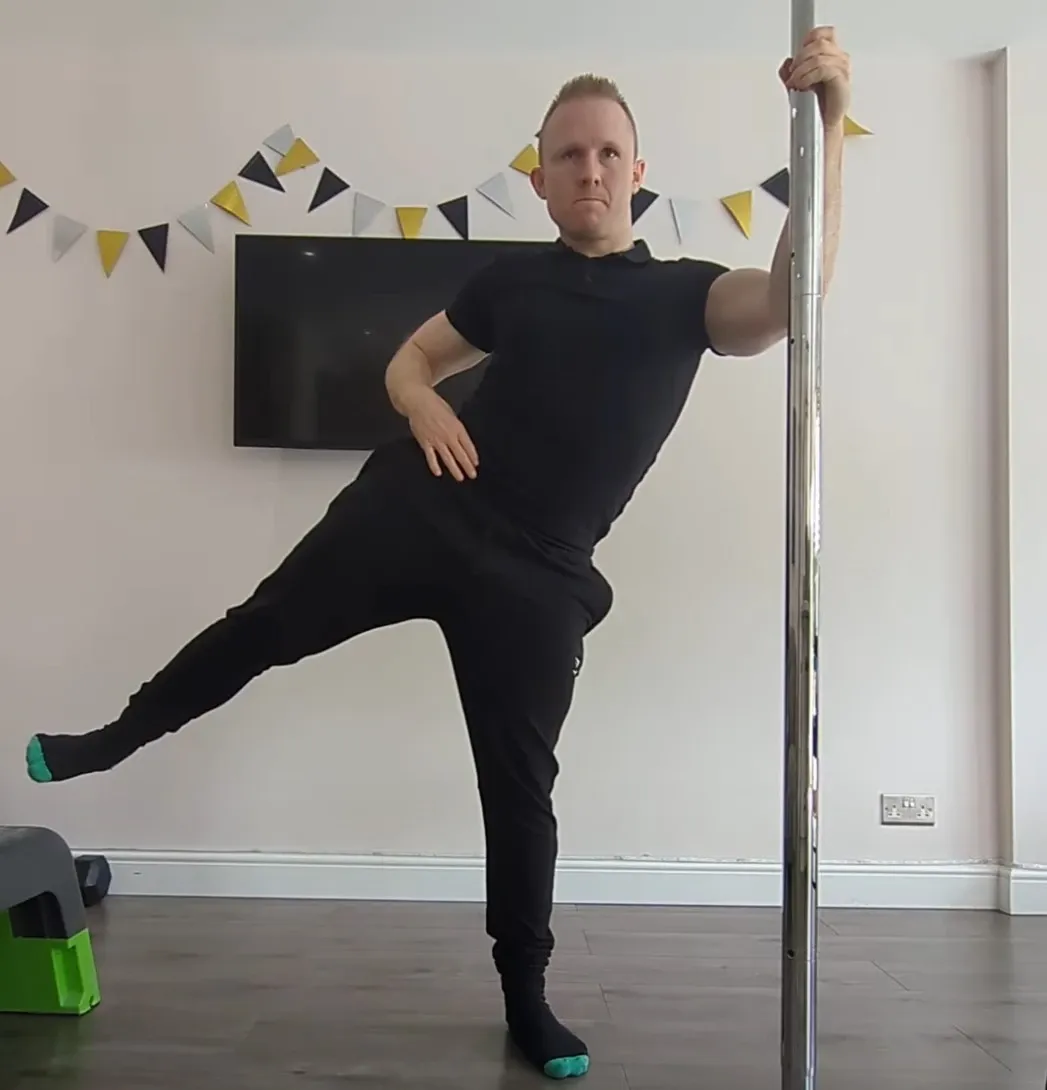 Andrew holding a pole with one hand while lifting his leg out to the side