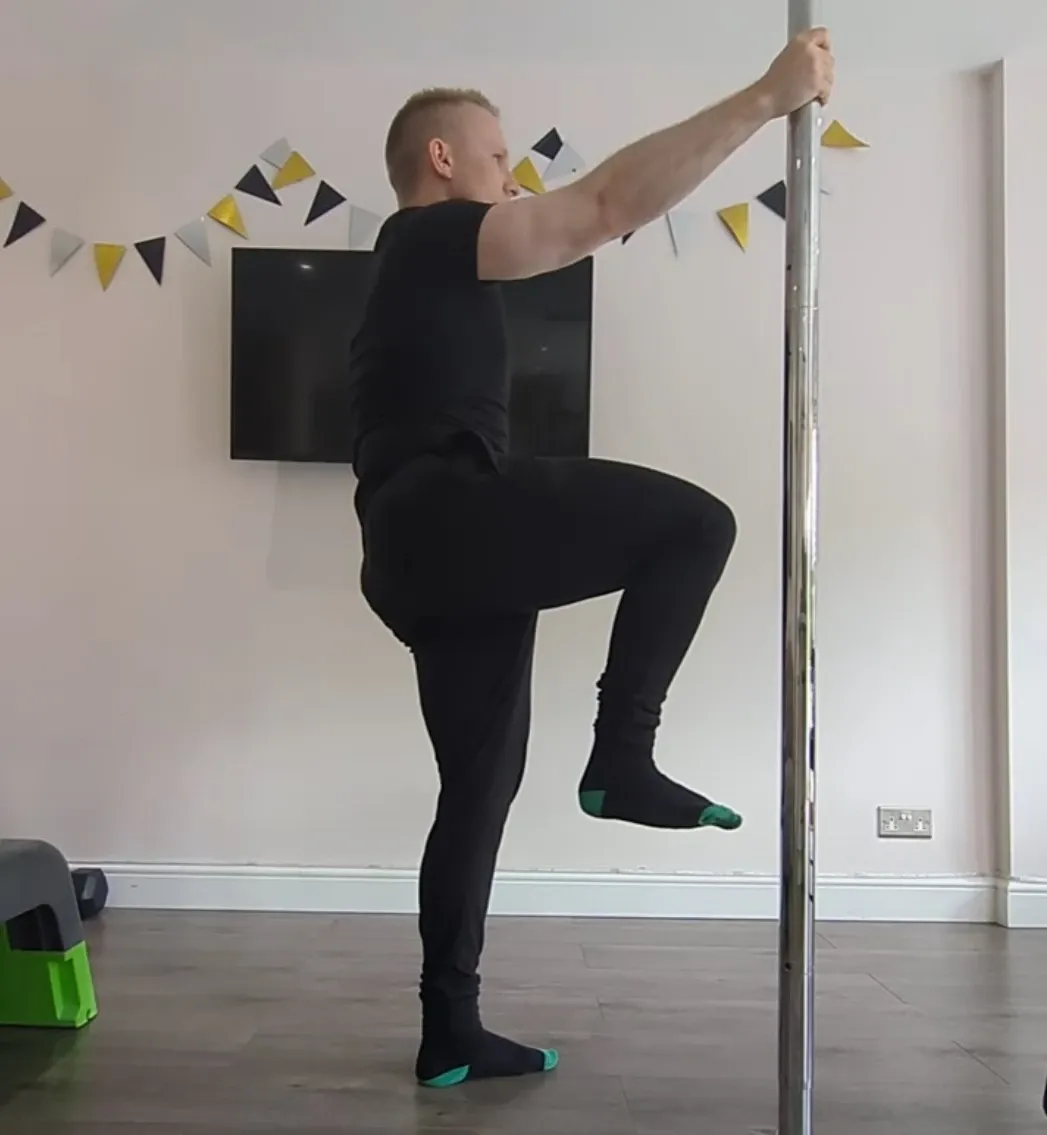 Andrew holding a pole while raising one knee to hip height