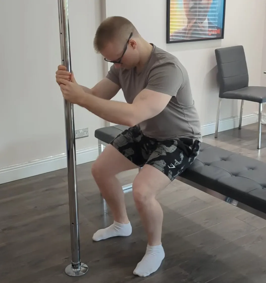 Andrew squatting down to a padded bench at home while holding a vertical pole for support